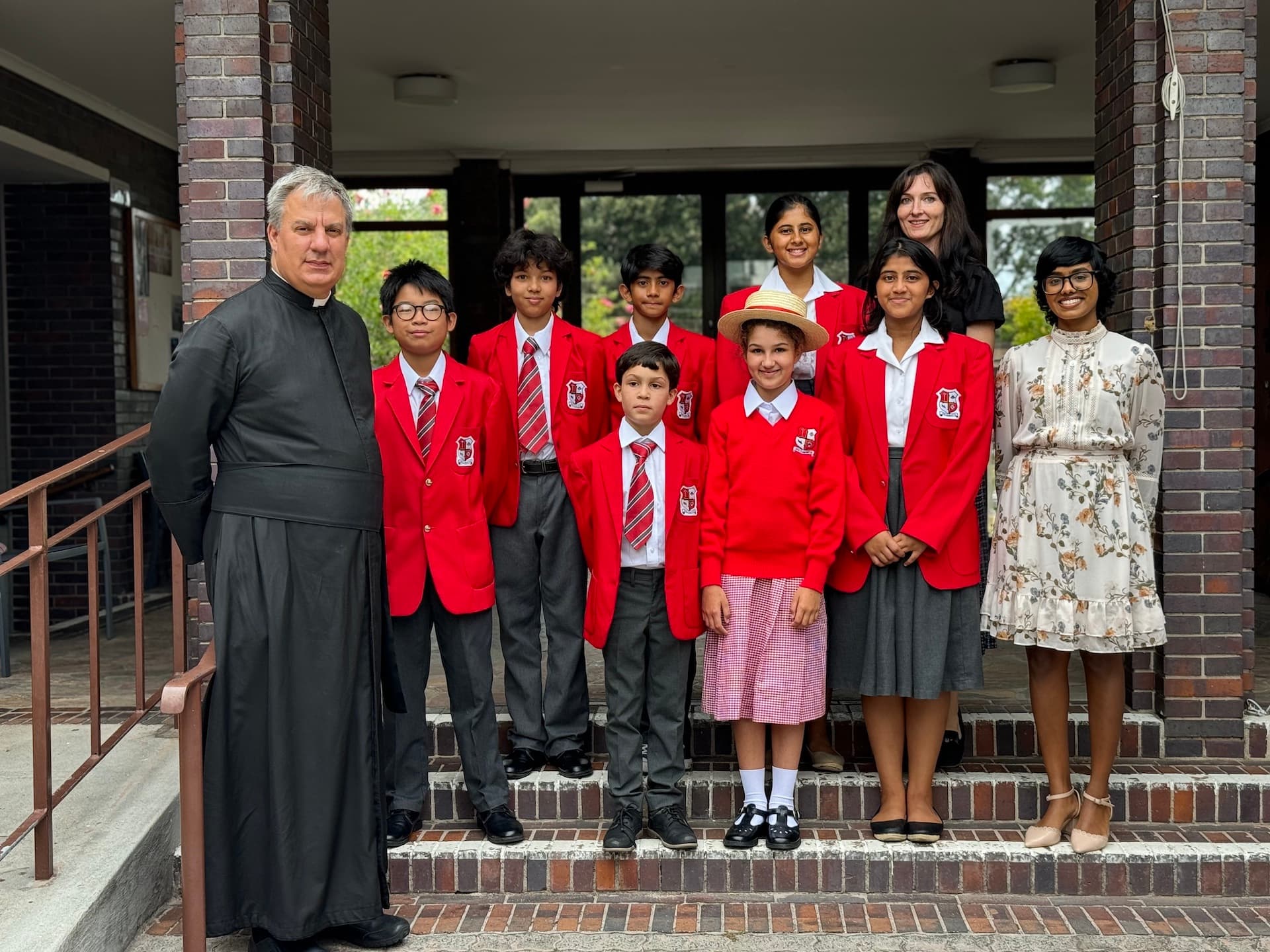 Pupils in red blazers with their priest and teachers on the chapel steps
